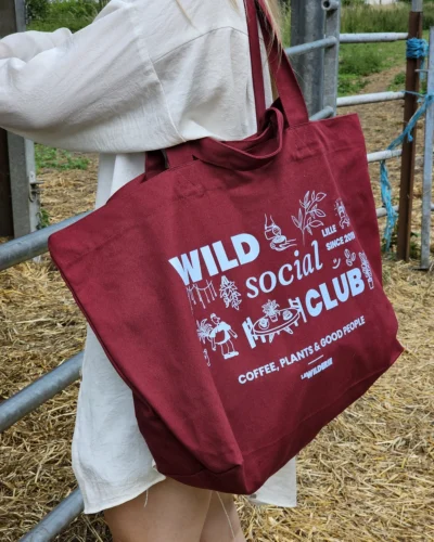 Tote bag bordeaux Wild Social Club La Wilderie porté à l'épaule, illustration café et plantes