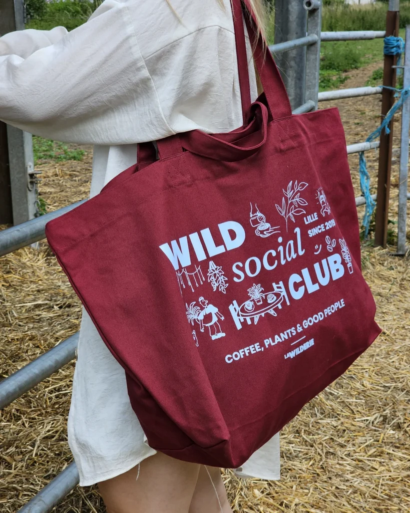 Tote bag bordeaux Wild Social Club La Wilderie porté à l'épaule, illustration café et plantes